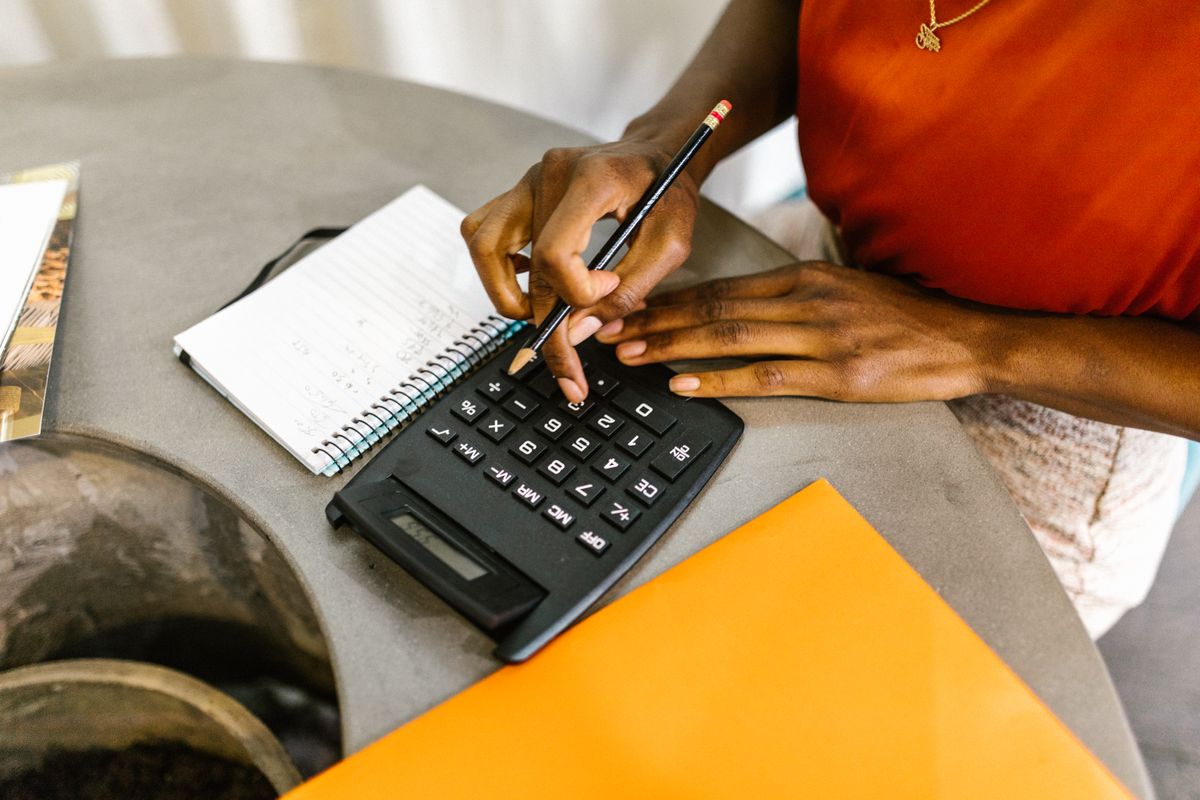 A person using a calculator beside a notebook to plan a budget.